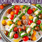 Caprese Salad Bites with heirloom cherry tomatoes, mozzarella balls, and fresh basil skewers on white plate with gray platter