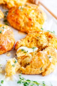 Cheddar Garlic Cornbread Biscuits with honey butter and fresh thyme on parchment paper and white marble