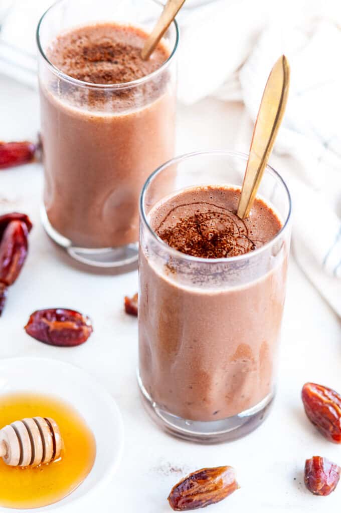 Dark Chocolate Date Smoothie with honey and gold spoons on white marble