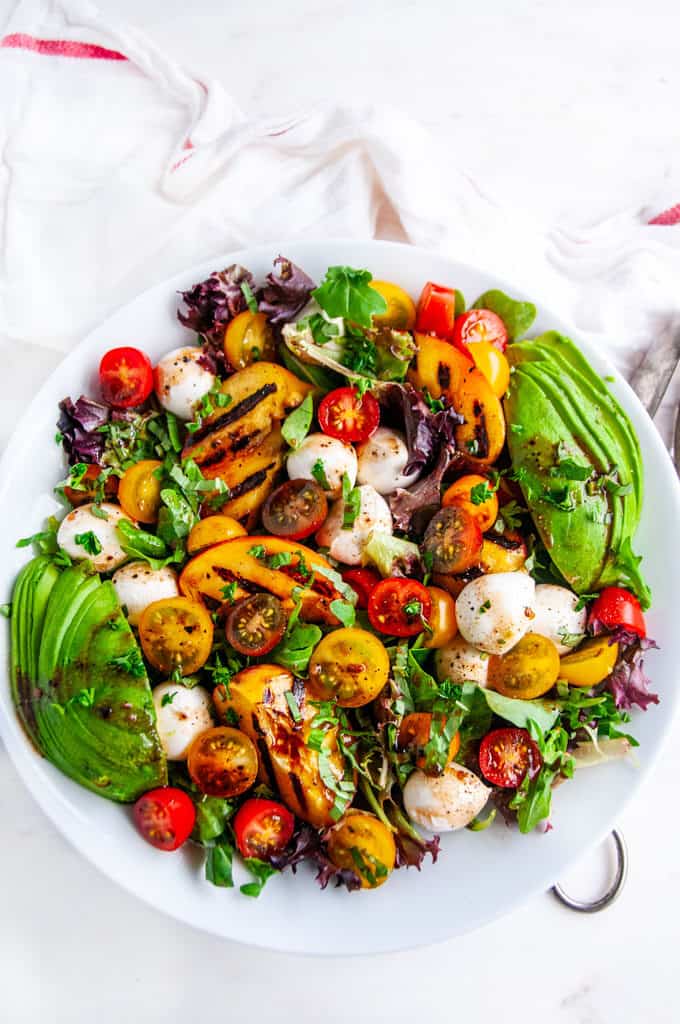 Grilled Peach Caprese Salad with avocado in white bowl on white marble