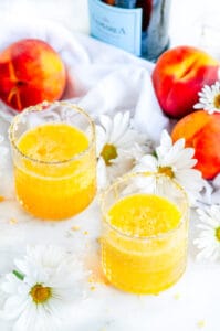 Fresh Peach Bellini Cocktail in glasses with sugared rim, white flowers and tea towel