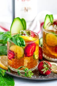 Classic Pimm's Cup Cocktail with lemon, cucumber, and strawberry slices garnished with basil leaves in glasses side view