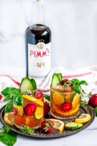 Classic Pimm's Cup Cocktail with lemon, cucumber, and strawberry slices garnished with basil leaves in glasses full view