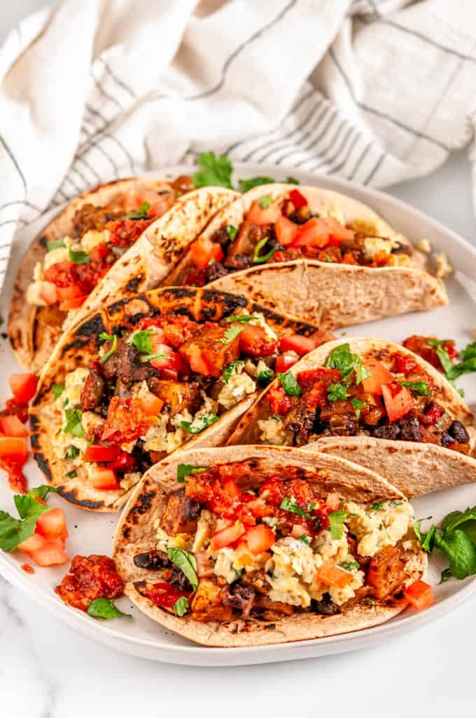 Loaded Vegetarian Breakfast Tacos with eggs, potatoes, black beans, salsa, and cilantro on white plate