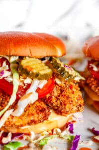 Panko Crusted Spicy Chicken Sandwiches with coleslaw, tomato, and pickles on white plate