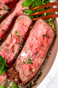 Easy Tender London Broil sliced on gray plate with fresh herbs