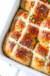 Everything Bagel Hot Cross Buns in white baking dish with sliced chives on white marble close up overhead view