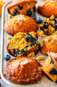 Zesty Orange Blueberry Muffins in silver muffin tray with sliced oranges and fresh blueberries on white marble side view close up