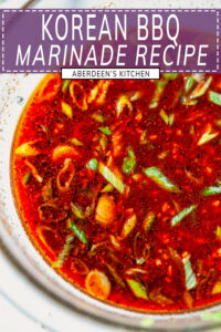 Korean BBQ Marinade whisked together in glass bowl on white marble with green onion and sesame seeds close up - purple rectangle overlay with white text