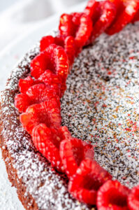 Chocolate Raspberry Flourless Cake sprinkled with powdered sugar on white cake stand close up view of the top