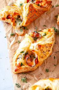 Cheesy Ham Spinach Puff Pastries on parchment paper and white marble with fresh thyme leaves close up