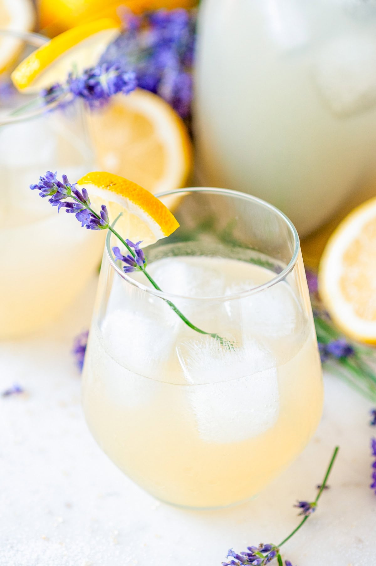 Boozy Lavender Lemonade Cocktail over ice in a wine glass with lavender sprig and lemon garnish