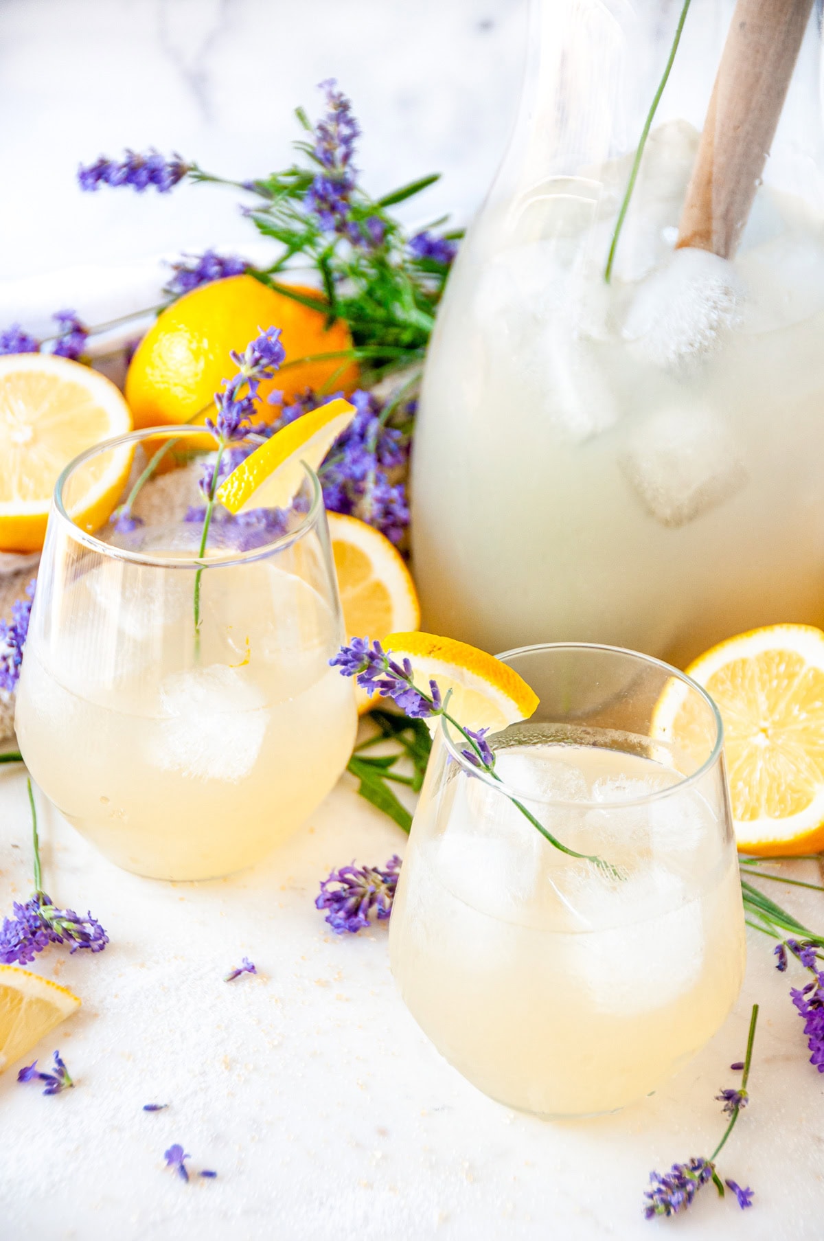 Boozy Lavender Lemonade Cocktail over ice in wine glasses with lavender sprigs and lemon garnish