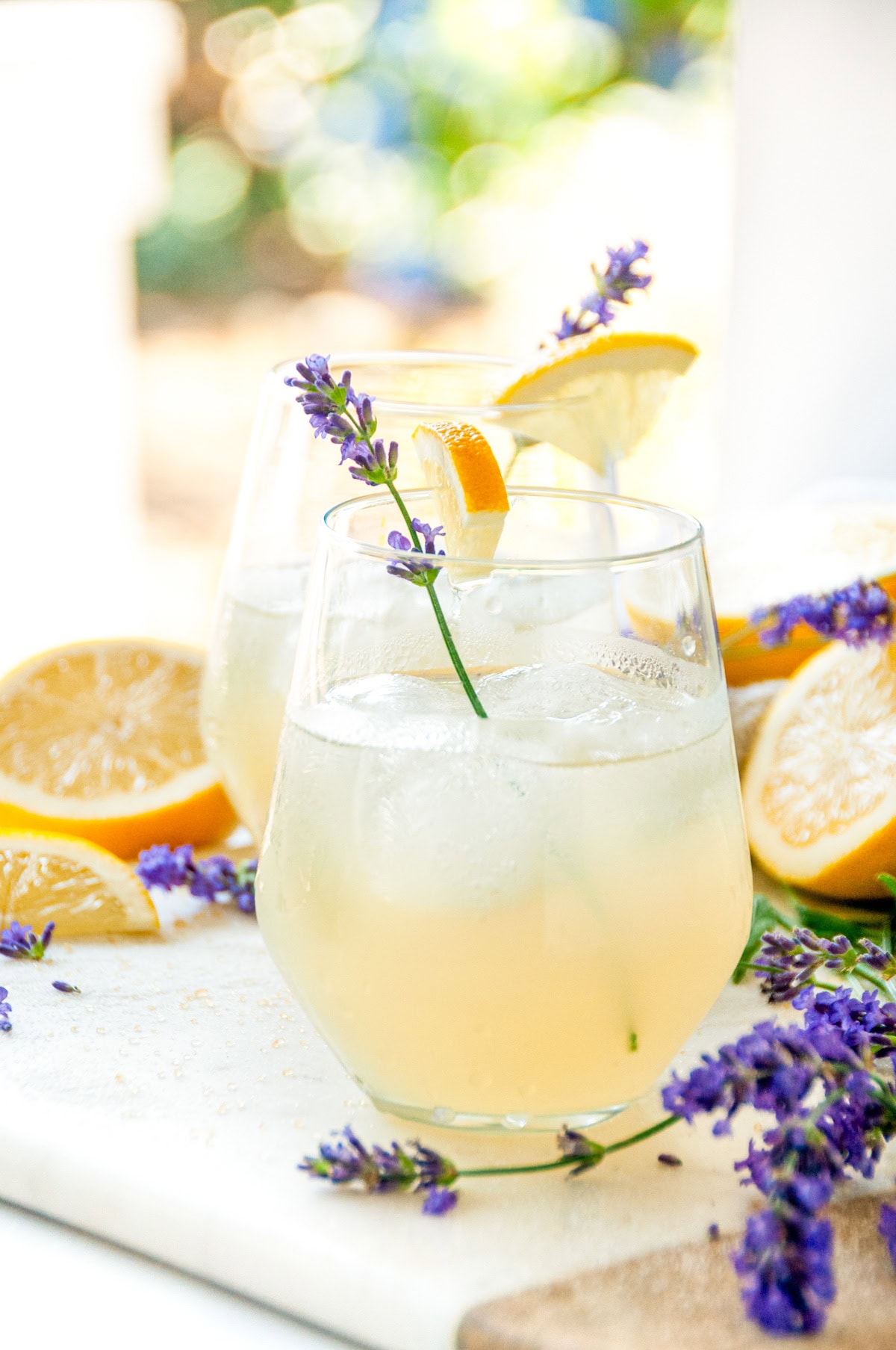 Boozy Lavender Lemonade Cocktail over ice in wine glasses with lavender sprigs and lemon garnish