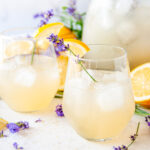 Boozy Lavender Lemonade Cocktail over ice in wine glasses with lavender sprigs and lemon garnish