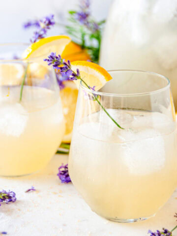 Boozy Lavender Lemonade Cocktail over ice in wine glasses with lavender sprigs and lemon garnish