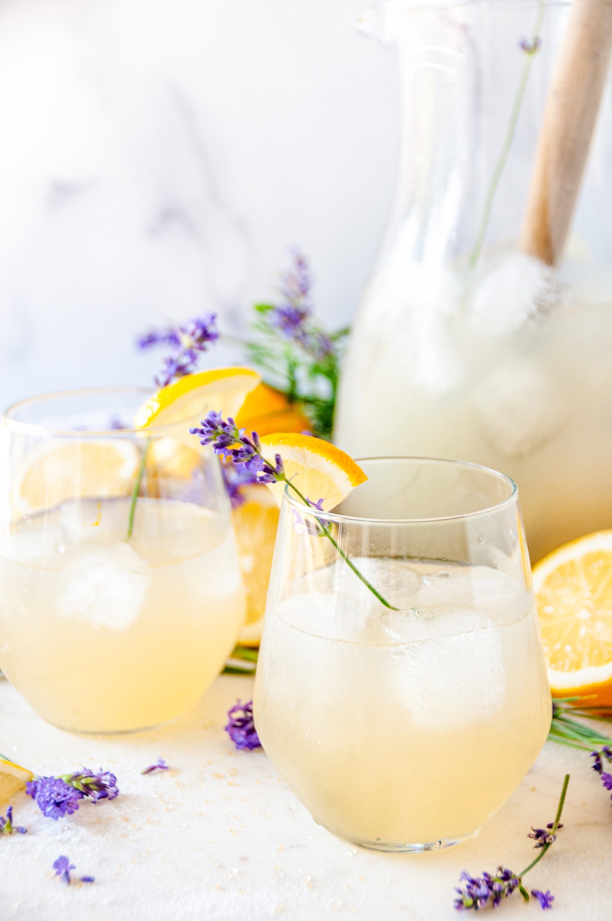 Boozy Lavender Lemonade Cocktail over ice in wine glasses with lavender sprigs and lemon garnish