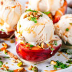 Grilled Peaches with Vanilla Ice Cream sprinkled with fresh mint and pistachios drizzled with caramel sauce on white marble