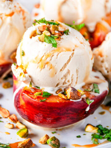 Grilled Peaches with Vanilla Ice Cream sprinkled with fresh mint and pistachios drizzled with caramel sauce on white marble