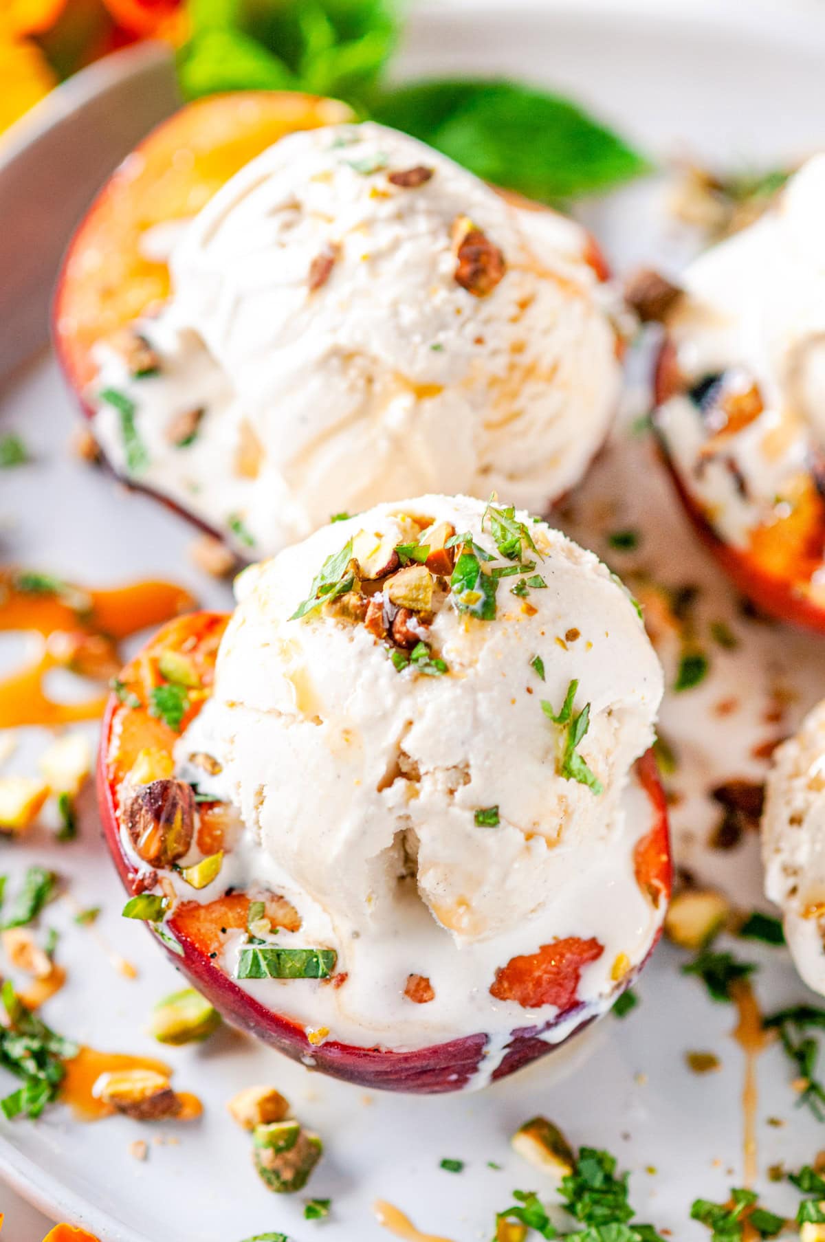 Grilled Peaches with Vanilla Ice Cream sprinkled with fresh mint and pistachios drizzled with caramel sauce on white marble